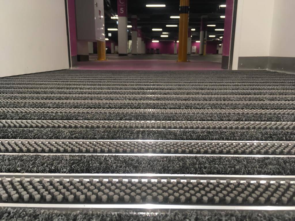 Entrance mat with gray brushes and gray ribbed carpet.